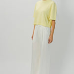 Side view of yellow cashmere cropped t-shirt on model wearing white pants, against a white background.