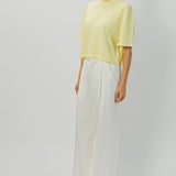 Side view of yellow cashmere cropped t-shirt on model wearing white pants, against a white background.
