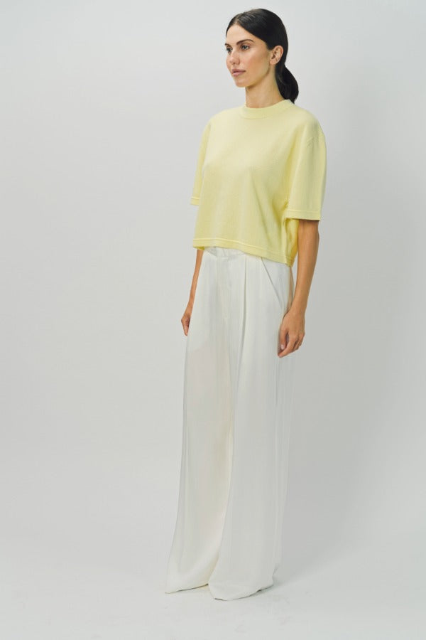 Side view of yellow cashmere cropped t-shirt on model wearing white pants, against a white background.