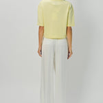 Back view of yellow cashmere cropped t-shirt on model wearing white pants, against a white background.