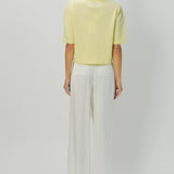 Back view of yellow cashmere cropped t-shirt on model wearing white pants, against a white background.