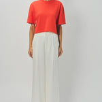 Front view of orange cashmere cropped t-shirt on model wearing white pants, against a white background.