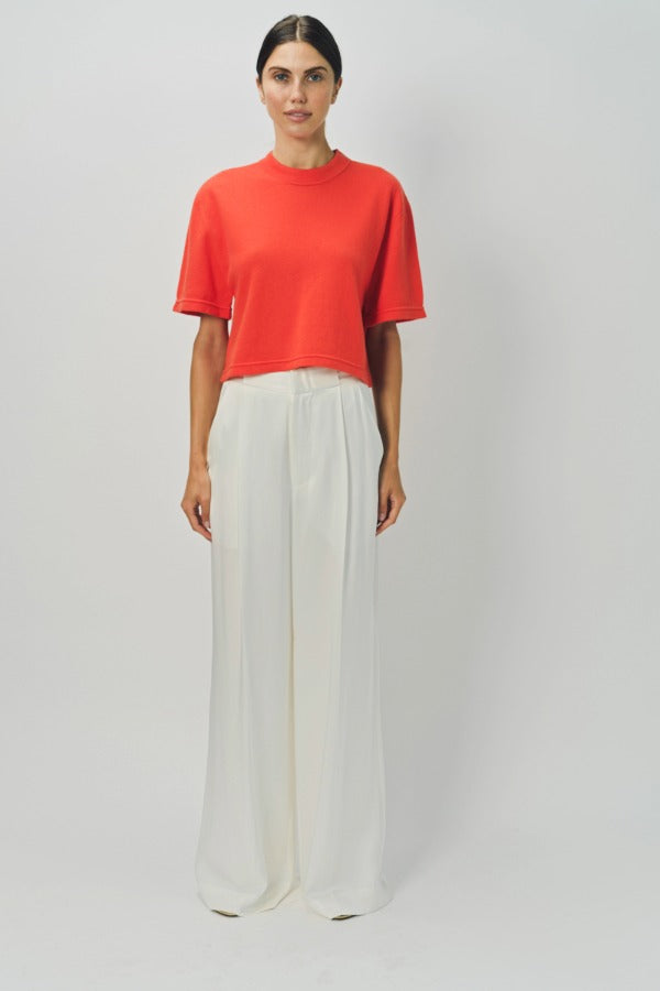 Front view of orange cashmere cropped t-shirt on model wearing white pants, against a white background.