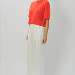 Side view of orange cashmere cropped t-shirt on model wearing white pants, against a white background.