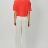 Back view of orange cashmere cropped t-shirt on model wearing white pants, against a white background.