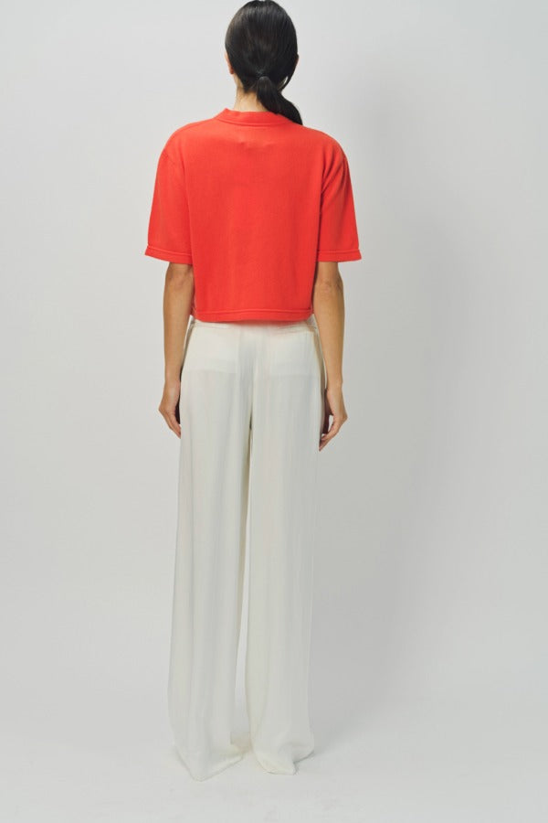 Back view of orange cashmere cropped t-shirt on model wearing white pants, against a white background.