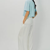Side view of cielo cashmere cropped t-shirt on model wearing white pants, against a white background.