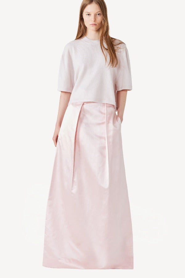 Front view of nude cashmere cropped t-shirt on model wearing pink skirt, against a white background.