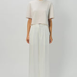 Front view of nude cashmere cropped t-shirt on model wearing white pants, against a white background.