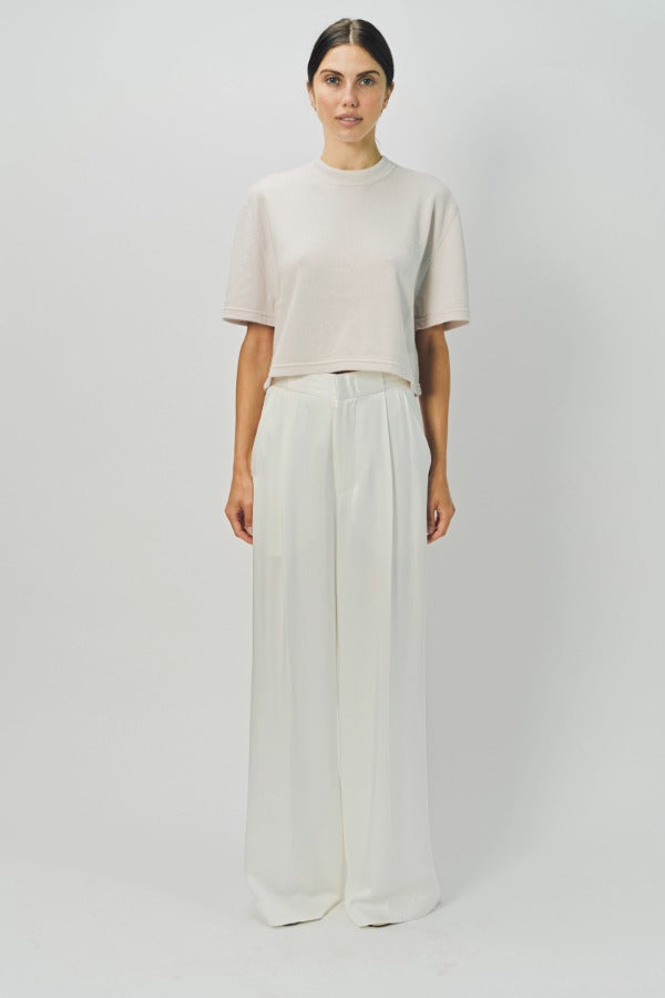 Front view of nude cashmere cropped t-shirt on model wearing white pants, against a white background.
