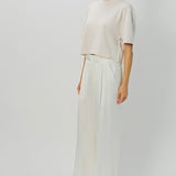 Side view of nude cashmere cropped t-shirt on model wearing white pants, against a white background.