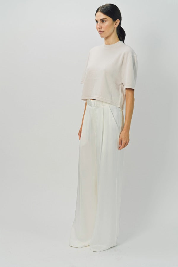 Side view of nude cashmere cropped t-shirt on model wearing white pants, against a white background.
