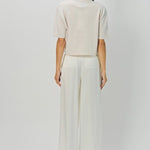 Back view of nude cashmere cropped t-shirt on model wearing white pants, against a white background.