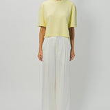 Front view of yellow cashmere cropped t-shirt on model wearing white pants, against a white background.