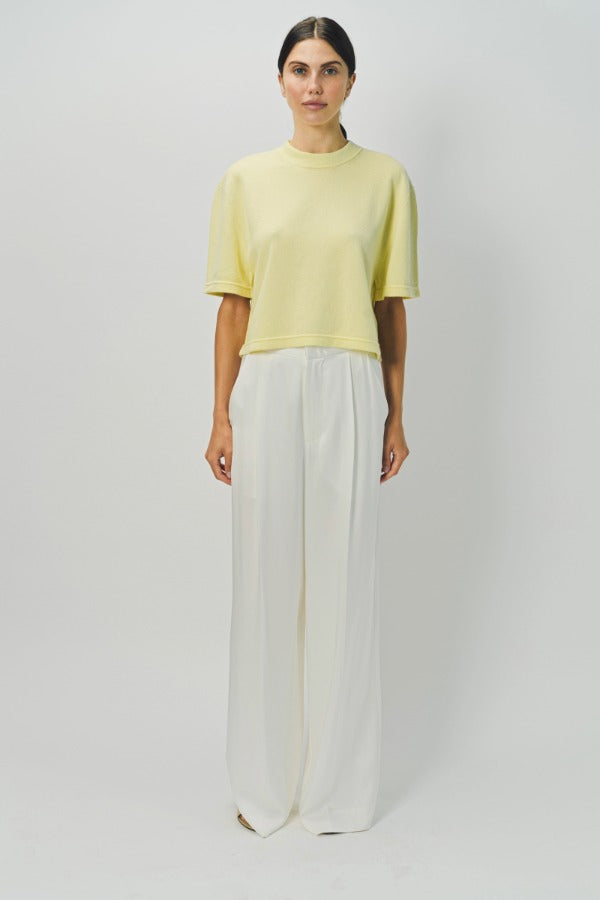 Front view of yellow cashmere cropped t-shirt on model wearing white pants, against a white background.