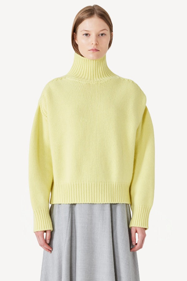 Front view of yellow cashmere high neck sweater on model wearing grey skirt