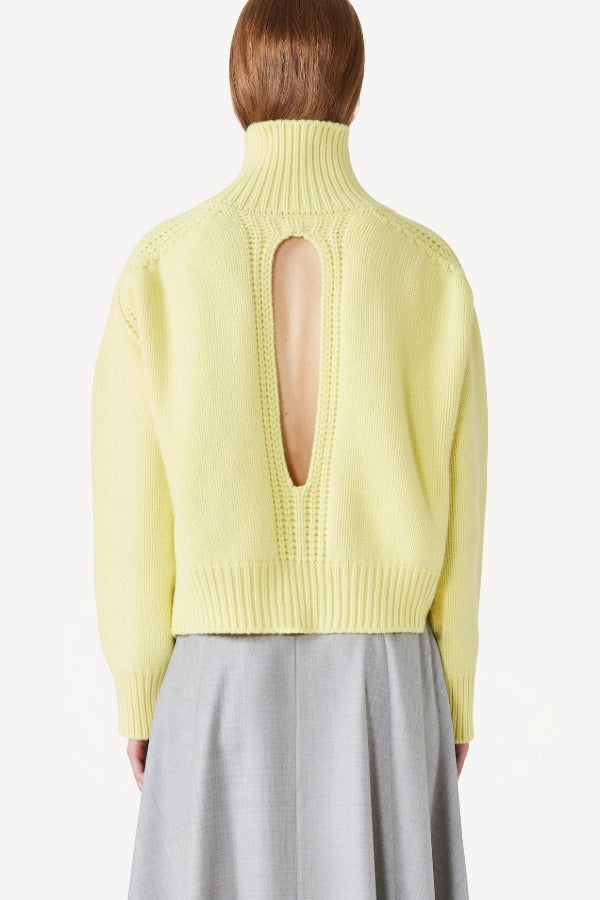 Back view of yellow cashmere high neck sweater on model wearing grey skirt, against a white background.