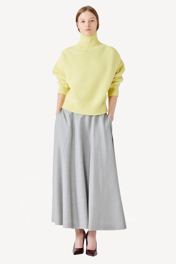 Front view of yellow cashmere high neck sweater on model wearing grey skirt, against a white background.
