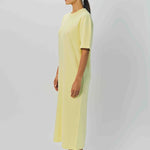 Side view of yellow cashmere long t-shirt dress on model wearing sandals, against a white background.