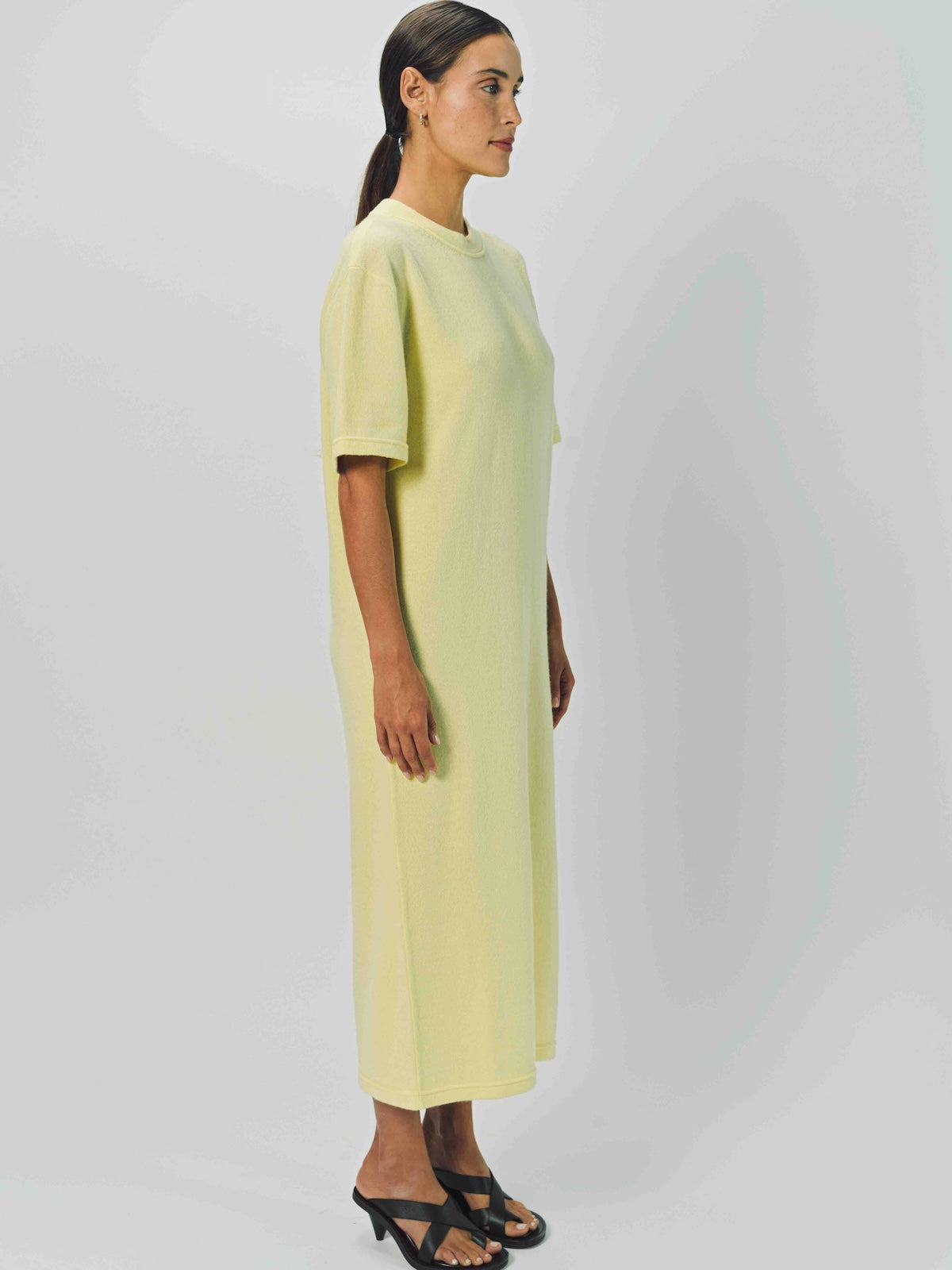 Alternate side view of yellow cashmere long t-shirt dress on model wearing sandals, against a white background.