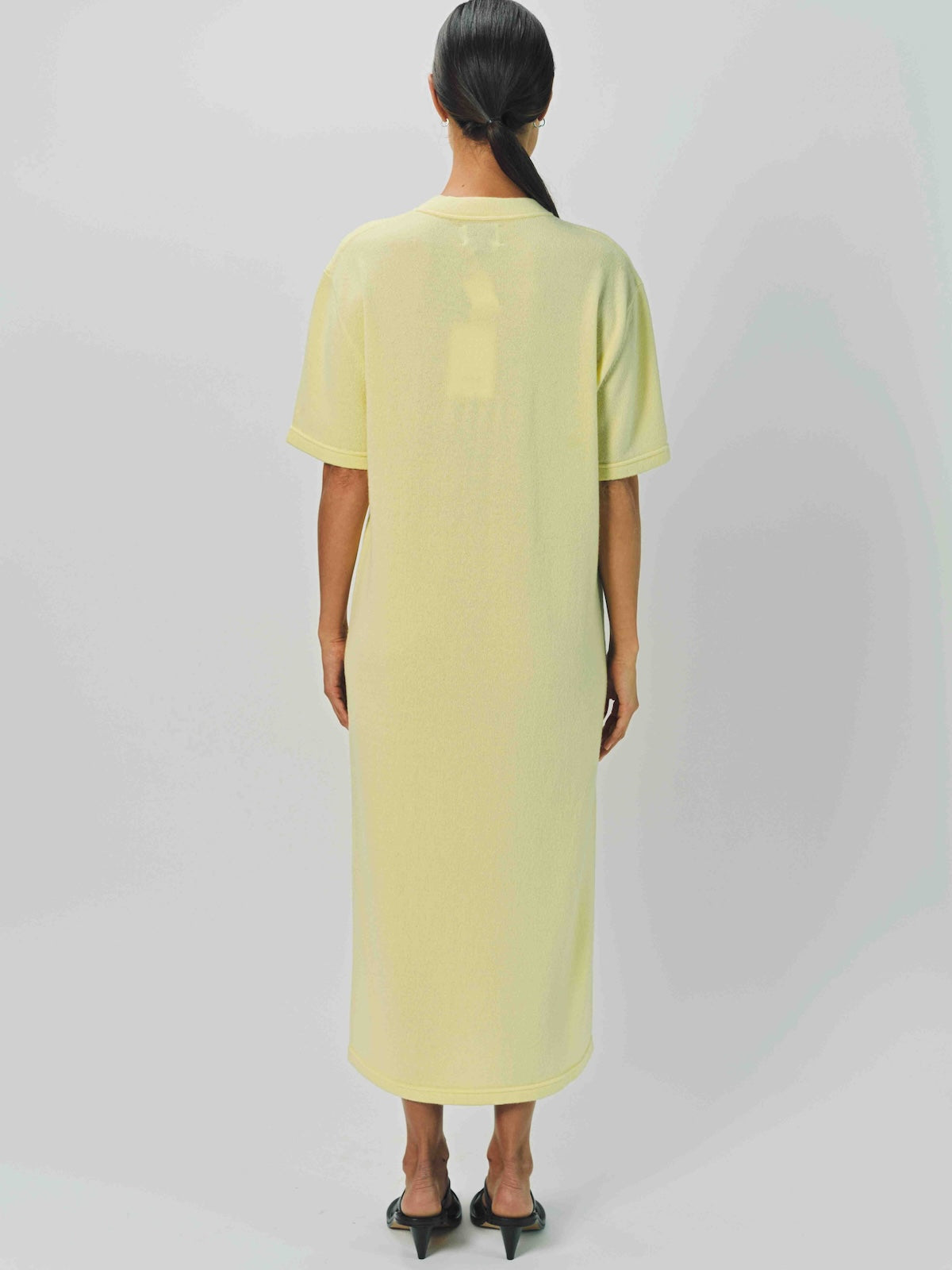 Back view of yellow cashmere long t-shirt dress on model wearing sandals, against a white background.