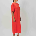 Side view of orange cashmere long t-shirt dress on model wearing sandals, against a  white background.