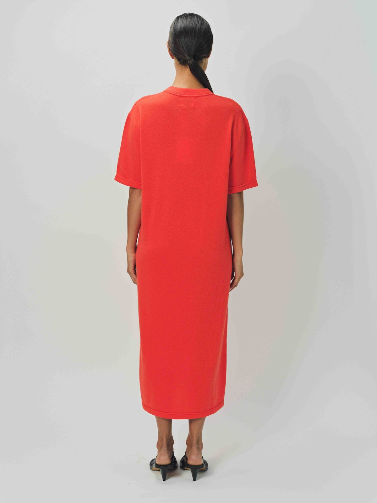 Back view of orange cashmere long t-shirt dress on model wearing sandals, against a white background.
