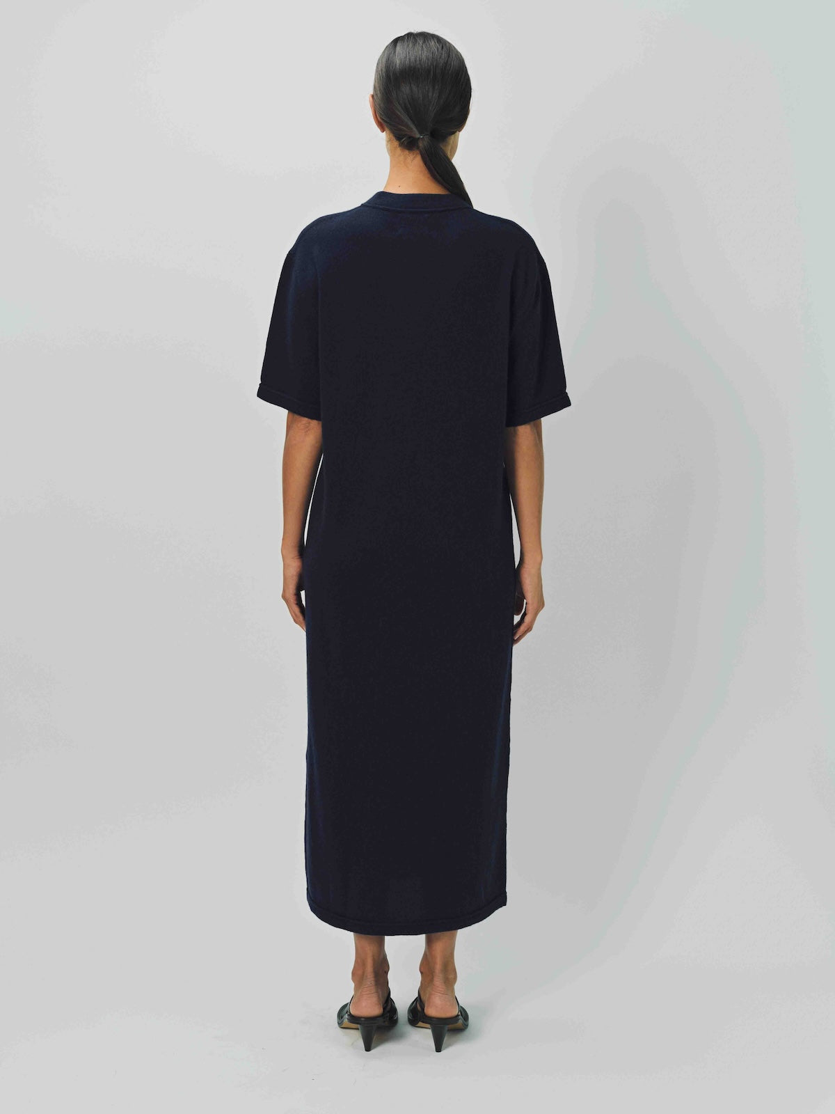 Back view of navy cashmere long t-shirt dress on model wearing sandals, against a white background.