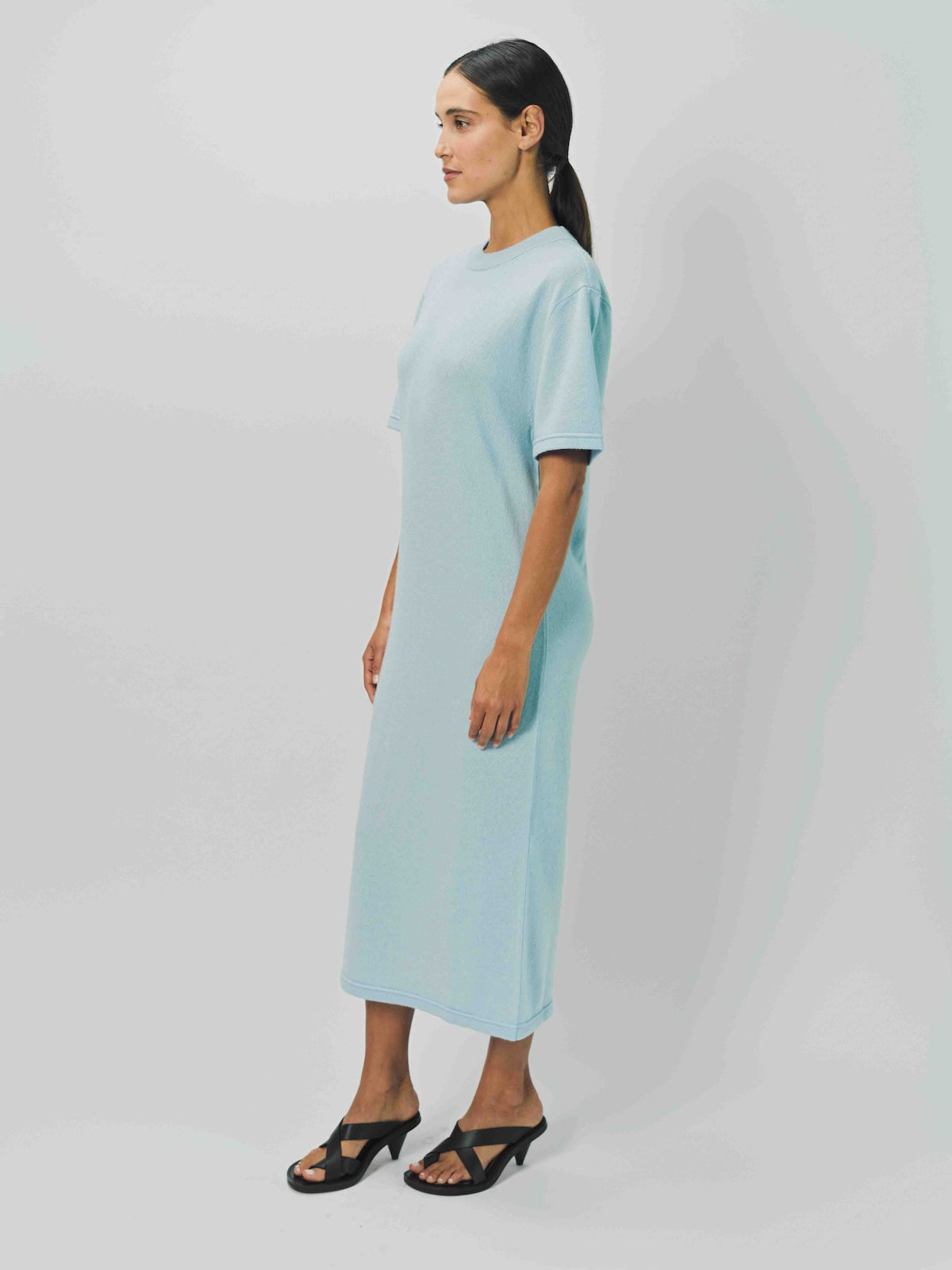 Side view of cielo cashmere long t-shirt dress on model wearing sandals, against a white background.