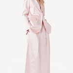 Side view of pink duchesse bogart long skirt on model wearing pink blazer, against a white background.