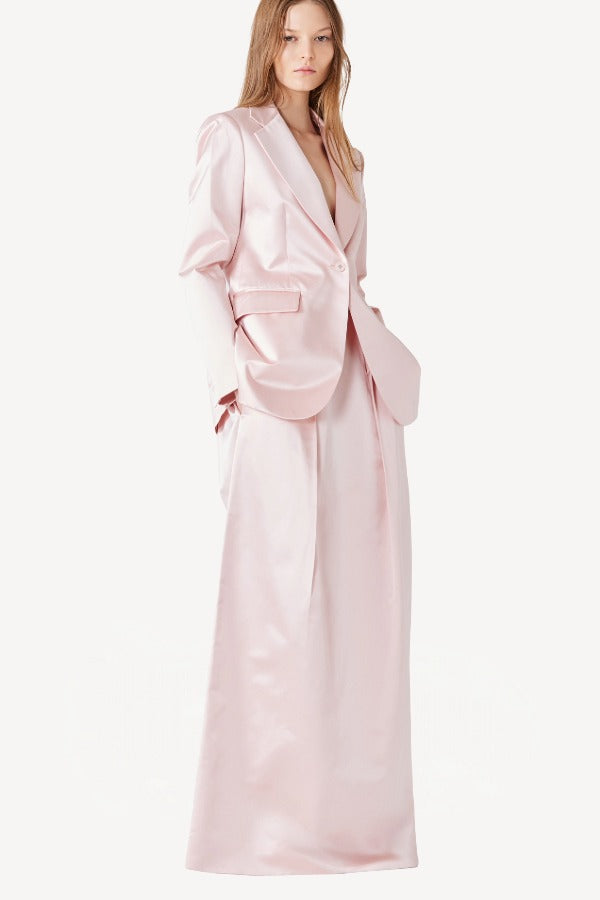 Side view of pink duchesse bogart long skirt on model wearing pink blazer, against a white background.