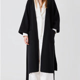 Open view of black isabella kimono coat on model wearing white top and pants, against a white bacgkround.