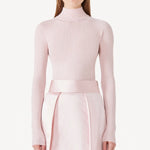 Front view of light pink cashmere l/s high neck sweater on model wearing pink skirt, against a white background.