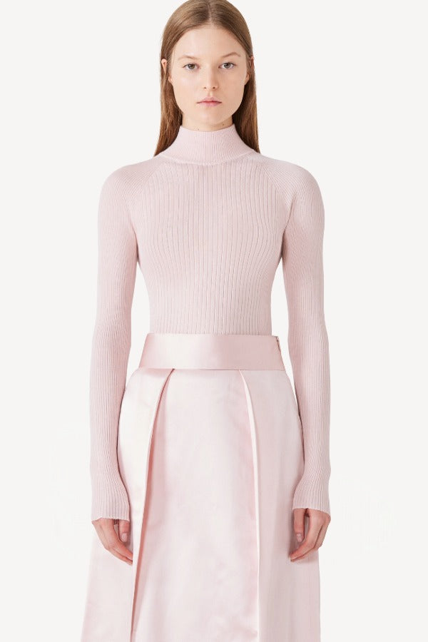 Front view of light pink cashmere l/s high neck sweater on model wearing pink skirt, against a white background.
