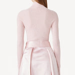 Back view of light pink l/s high neck sweater on model wearing pink skirt, against a white background.