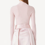Back view of light pink l/s high neck sweater on model wearing pink skirt, against a white background.