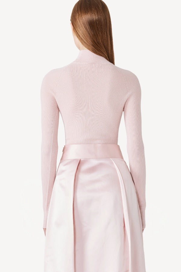 Back view of light pink l/s high neck sweater on model wearing pink skirt, against a white background.