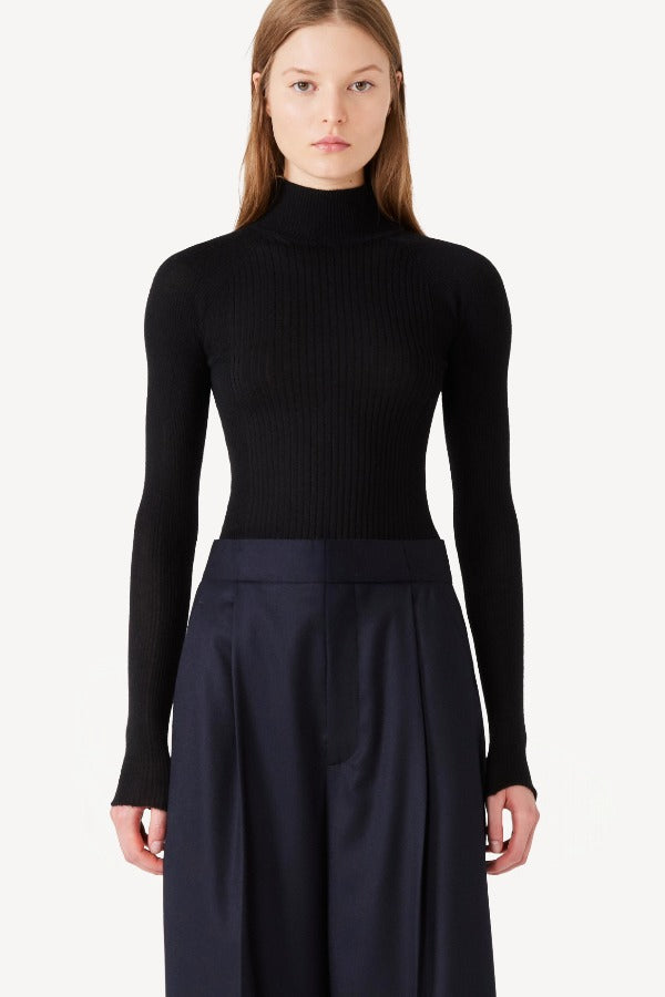 Front view of black l/s cashmere high neck sweater on model wearing navy pants, against a white background.