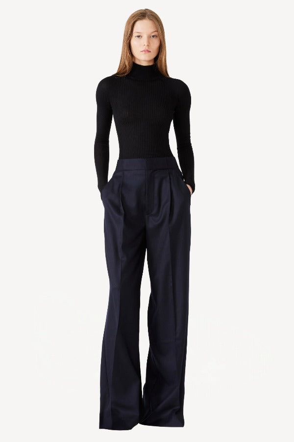 Front view of black l/s cashmere high neck sweater on model wearing navy pants, against a white background.