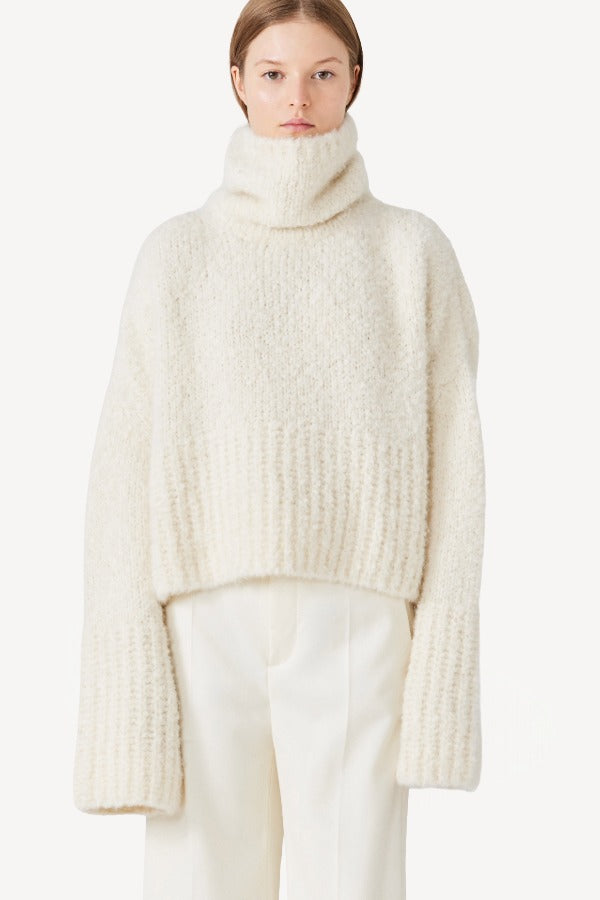 Front view of ivory l/s high neck cashmere sweater on model wearing white pants, against a white background.