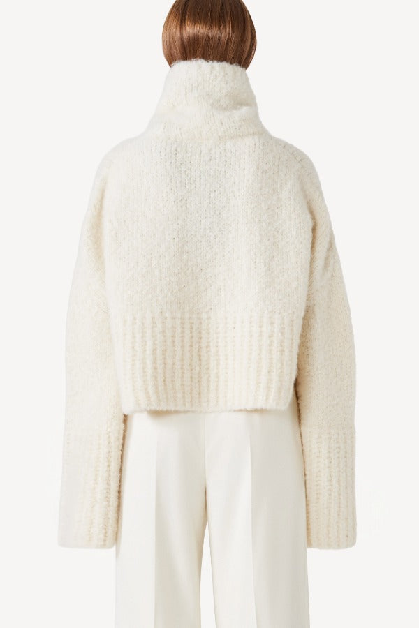 Back view of ivory l/s high neck cashmere sweater on model wearing white pants, against a white background.