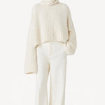 Front view of ivory l/s high neck cashmere sweater on model wearing white pants, against a white background.