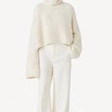 Front view of ivory l/s high neck cashmere sweater on model wearing white pants, against a white background.