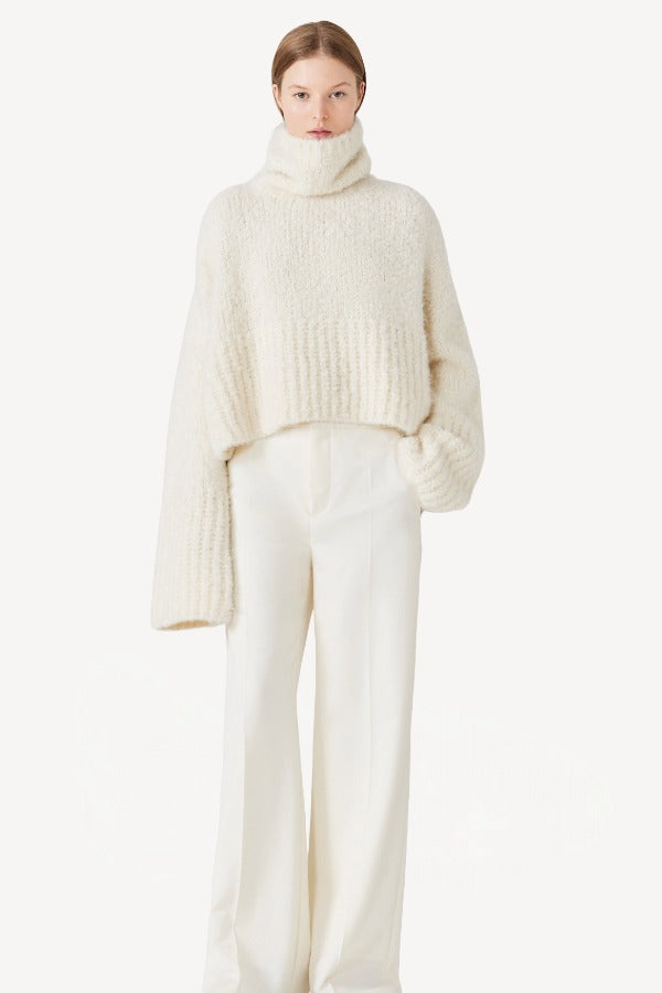 Front view of ivory l/s high neck cashmere sweater on model wearing white pants, against a white background.