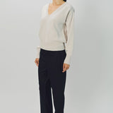 Side view of nude lavina v-neck cashmere sweater on model wearing black pants and flats, against a white background.
