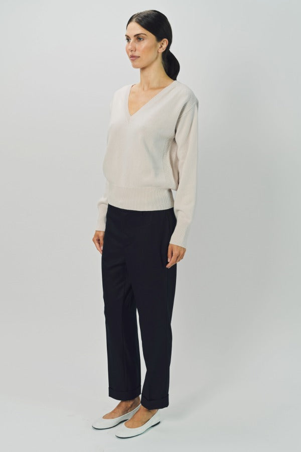 Side view of nude lavina v-neck cashmere sweater on model wearing black pants and flats, against a white background.
