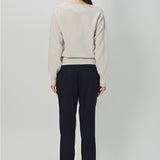 Back view of nude lavina v-neck cashmere sweater on model wearing black pants and flats, against a white background.