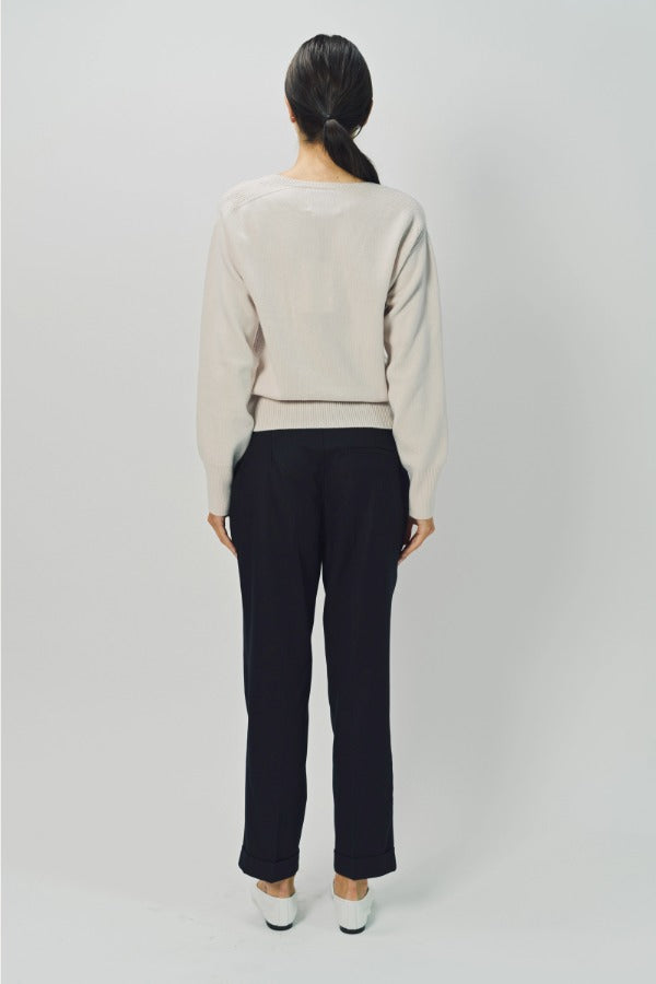 Back view of nude lavina v-neck cashmere sweater on model wearing black pants and flats, against a white background.