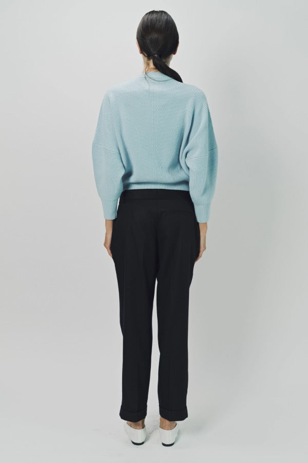 Back view of cielo mina cashmere bat wing sweater on model wearing bladck pants and flats, against a white background.