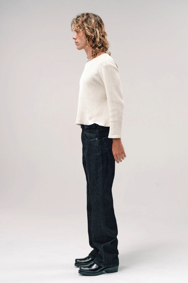 Side view of black big papi denim pants on model wearing white shirt and boots, against a white background.